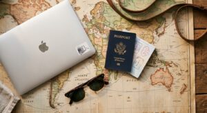 A flat-lay professional photograph of a laptop, a passport, and a pair of sunglasses resting on a wo