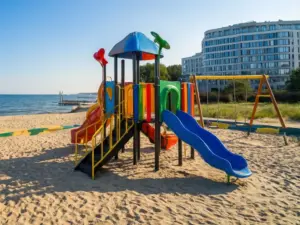Plac zabaw przy hotelu dla dzieci nad morzem z kolorowymi zjeżdżalniami i piaszczystą plażą w tle